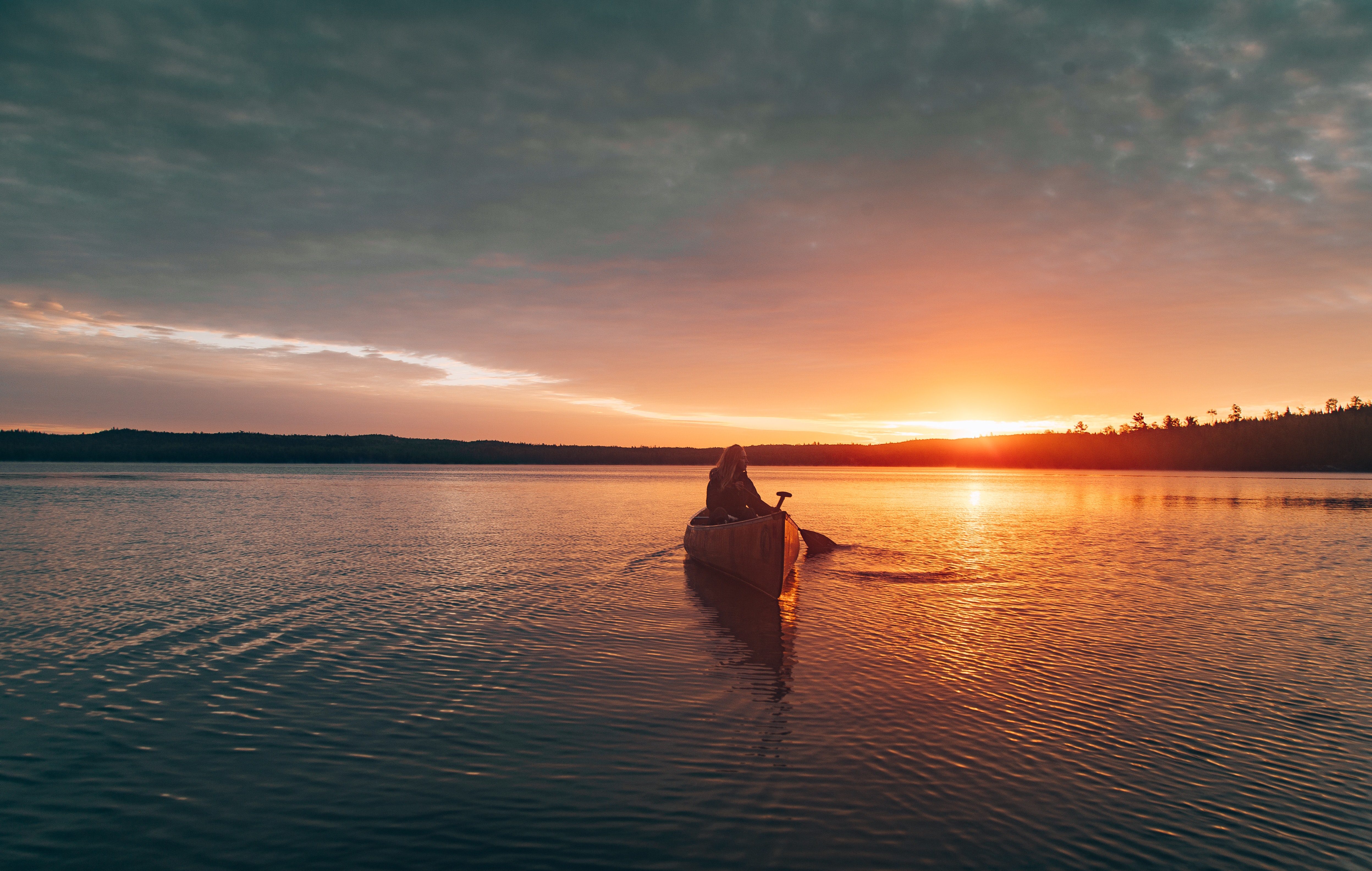 boater in a canoe on the lake at sunset paddling towards the camera